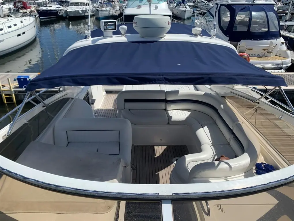 Aerial view of a boat's deck featuring white seating, a blue canopy, and surrounding boats in a marina.